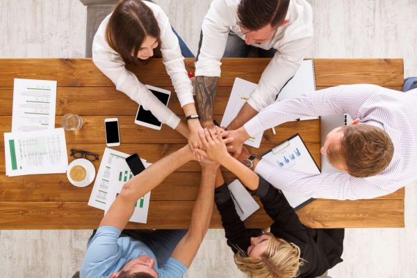 Team put hands together, show connection and alliance. Teambuilding in the office, young businessmen and women in casual unite hands for teamwork and cooperation at project. Top view, overhead